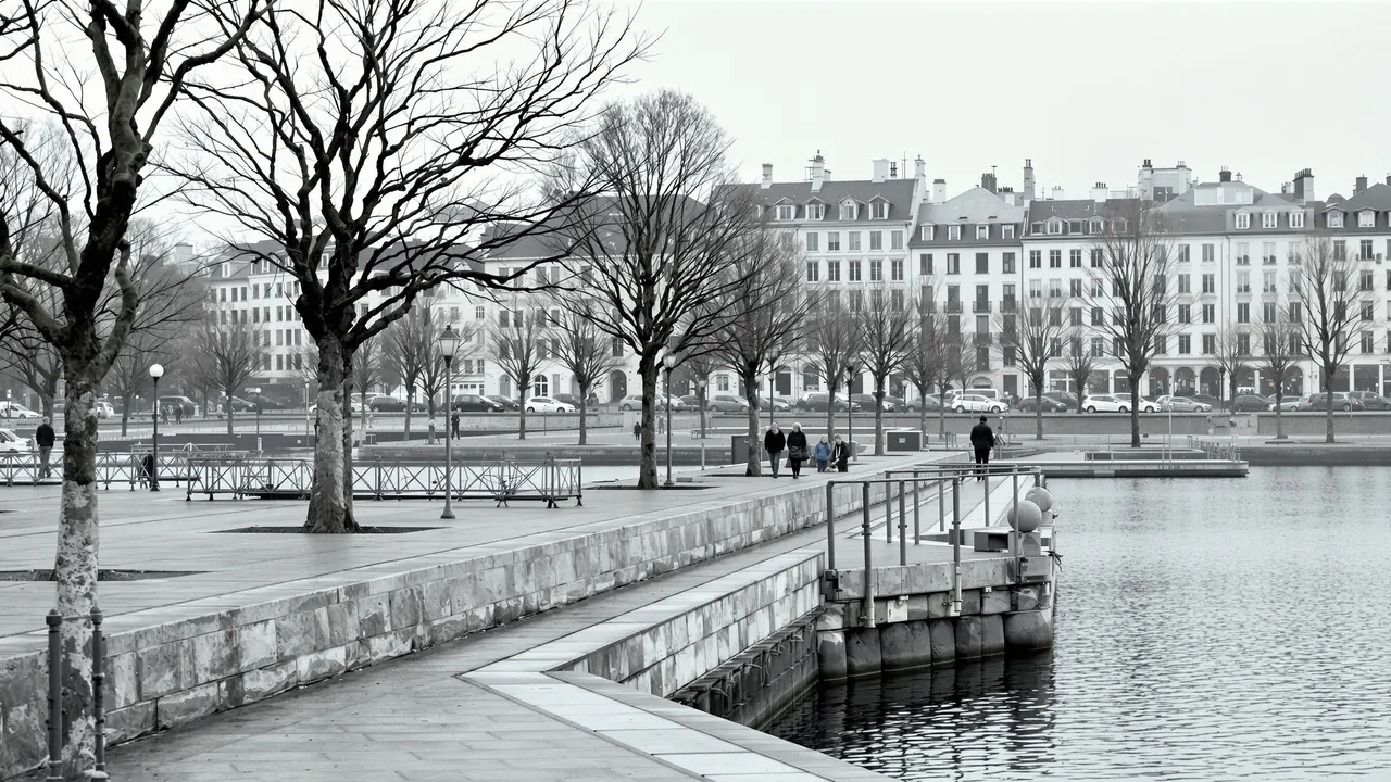 Eine Seepromenade in einer Schweizer Stadt an einem grauen Tag, gepflasterter Weg mit niedriger Steinbrüstung und kahlen Platanen an stillem grauem Wasser