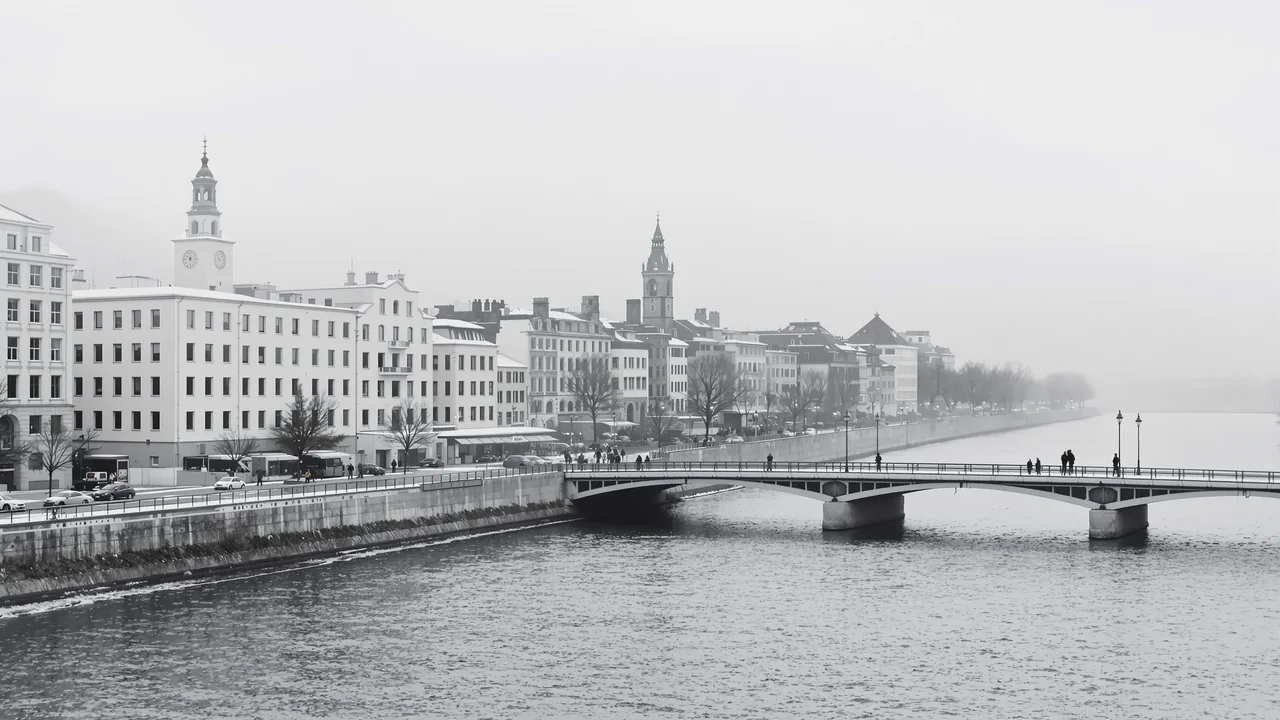 Ein Rheinübergang bei Basel im flachen Winterlicht, schlichte helle Bürobauten und ältere Steinfassaden an beiden Ufern, davor breites graues Wasser
