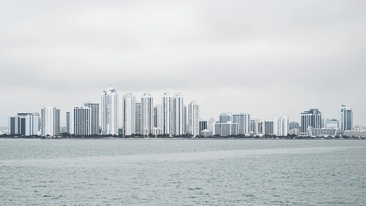 Die Hochhäuser des Bankenviertels von Panama-Stadt hinter einer weiten, ruhigen Bucht bei bedecktem Himmel